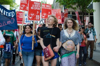 A couple walks hand in hand with an anti-corporate message written on the woman’s stomach. (Photo by Seth Halleran)