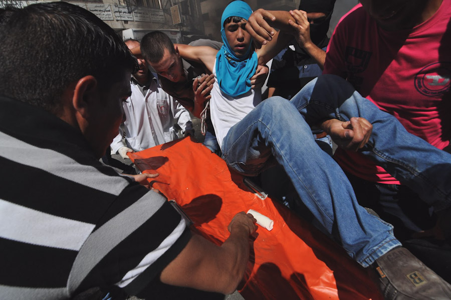 Protesters carry a wounded teenager to a waiting stretcher after a protest in Hebron devolved into clashes between stone throwers and Israeli soldiers. (Photo by Tom James)