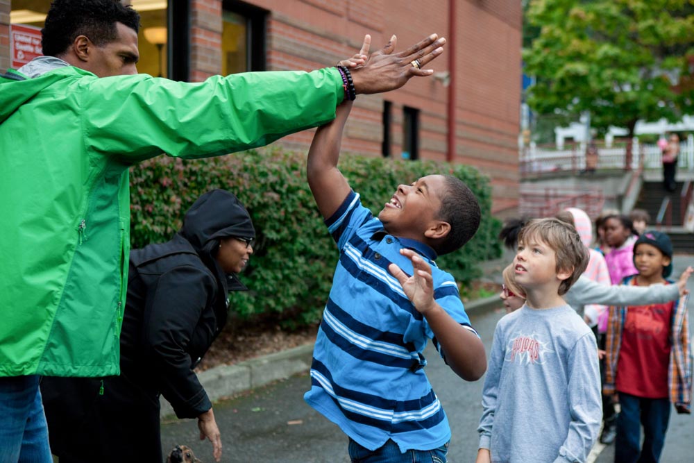 Gabriel Ray Pierre (left) high fives a student at Leschi Elementary School on Friday, as part of #SeattleHigh5. The event aimed to show children of color positive images of black men and women in their community. (Photo by Jovelle Tamayo)