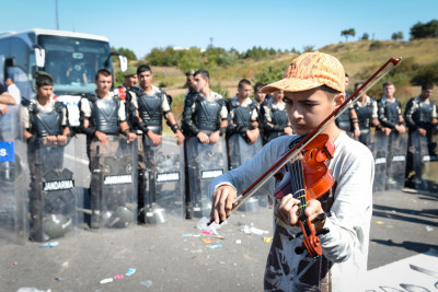 A young refugee plays violin in front of a line of Turkish police at Edirne, where refugees amassed hoping to cross into Bulgaria. (Photo by Levent ......)