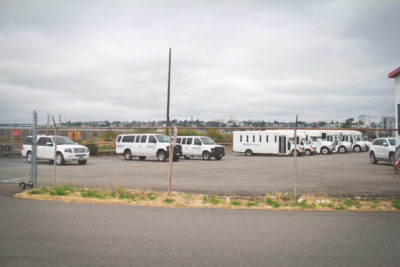 Vans and busses used to transport detainees and detention center staff are parked across from the NWDC. The facility is owned and operated by a private corporation called The GEO Group. (Photo by Damme Getachew)