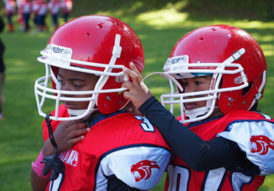 A South West Athletics Club Cougar helps his teammate with his helmet before a 2013 game against the Rainier Eagles.