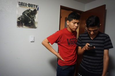 Ricardo looks at something at his phone while his brother Jonathan watches alongside him. (Photo by Agatha Pacheco)