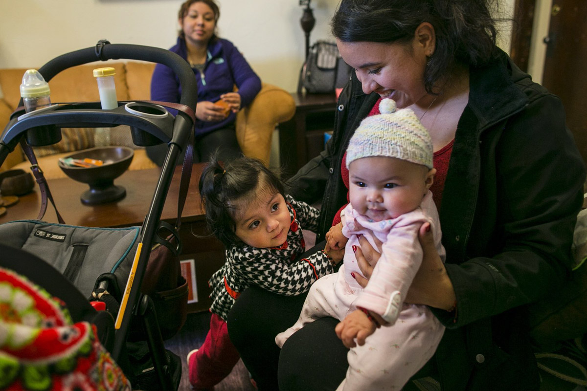 Martha Langarica, right, holds her 4-month-old daughter, Mia, as Evelyn Reyes, 16 months old, takes a closer look. The families were visiting Open Arms Perinatal Services to get advice from the doulas and personnel at the center, as well as diapers. (Photo by Johnny Andrews / The Seattle Times)